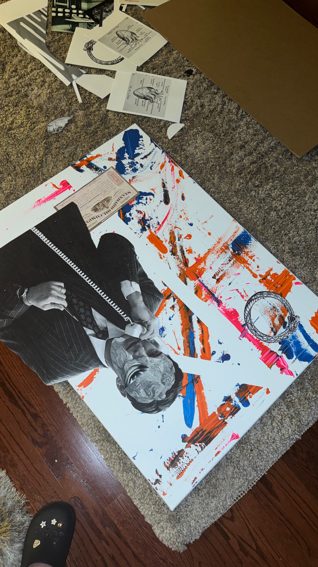 Paper engravings, cutouts and orange and blue paint arranged on a work-in-progress canvas